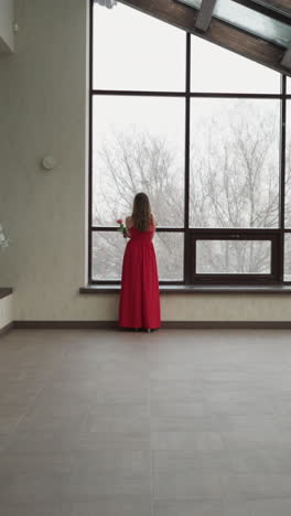 una mujer pensativa se encuentra cerca de la ventana de la terraza. una mujer joven trae un aura de sofisticación al entorno del estudio de arte mirando con gracia el paisaje de invierno