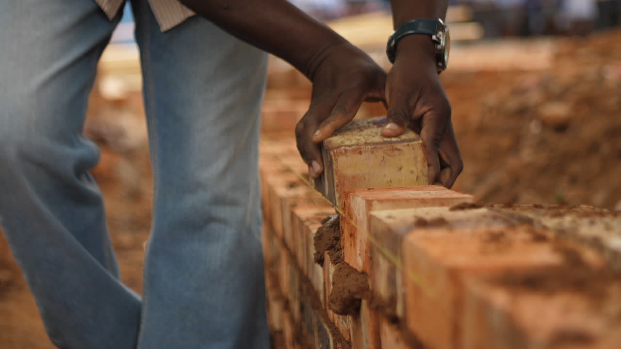 Black construction worker places bricks in wall with cement
