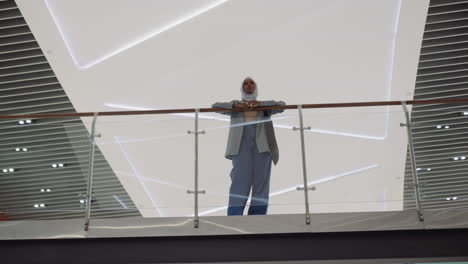 young black woman leans on glass railing in shopping mall