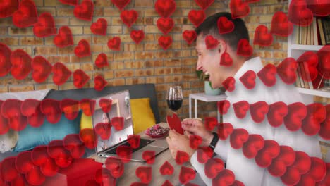 iconos del corazón contra el hombre caucásico sosteniendo un cartel en forma de corazón mientras hace una videollamada en una computadora portátil
