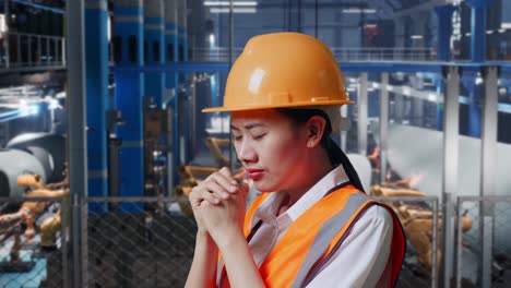 close up side view of asian female engineer with safety helmet prays for something while standing in factory manufacture of wind turbines