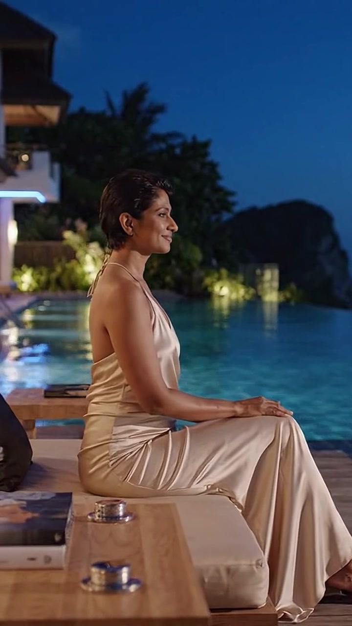 Mujer elegante con vestido de satén junto a una piscina infinita de noche, capturando la belleza serena y la tranquilidad en un entorno lujoso bajo un cielo iluminado por la luna.