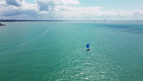 drone footage follows a sailboat sailing across the coastal waters of normandy, with mont saint-michel appearing slowly on the horizon
