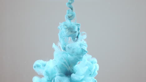 blue paint squirted into clear liquid on grey background, slow motion