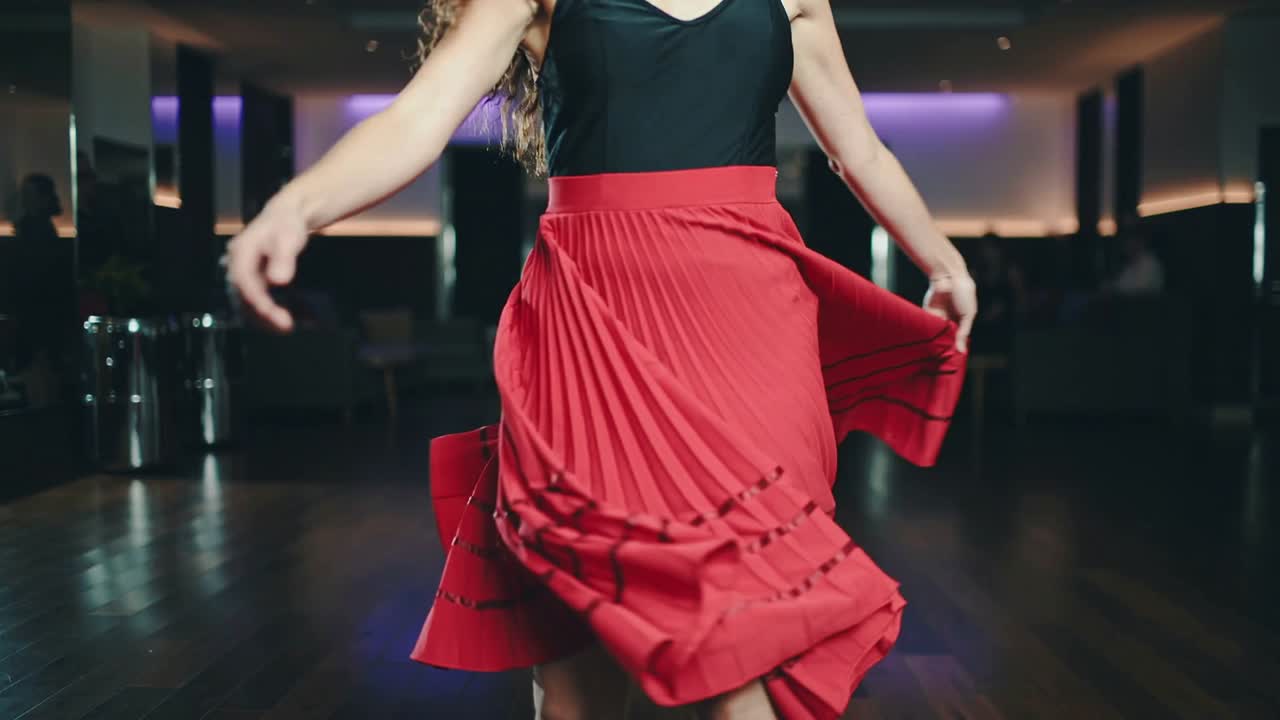 Spinning woman dancer practicing twirl in studio, wearing black top and red pleated skirt flaring