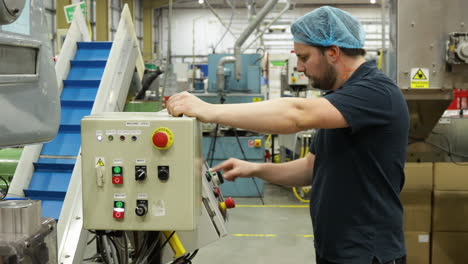 un trabajador de la fábrica de almacén masculino presiona los botones en un panel de control de la máquina en el centro de operaciones