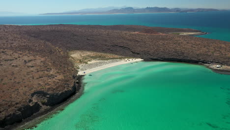 Cinematic-drone-shot-of-Balandra-Beach,-passing-over-the-red-hills,-turquoise-waters-and-white-sand-beaches,-wide-rotating