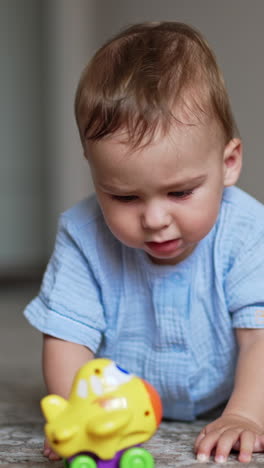 nice cute baby boy in blue clothes stands on all fours on the floor. lovely kid tries to choose a toy in front of him. blurred backdrop. vertical video