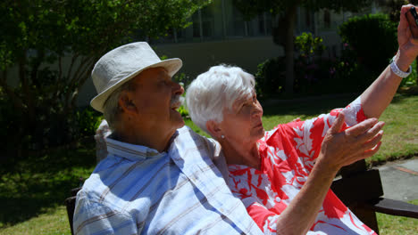 vista frontal de una pareja de ancianos caucásicos activos tomando selfies con el teléfono móvil en el jardín de la enfermera