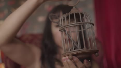 close up video of a woman with the dark red lipstick spinning a small metal cage with a large key inside