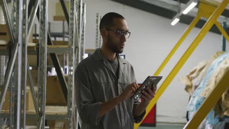 mecánico de automóviles afroamericano de pie en un almacén y usando una tableta