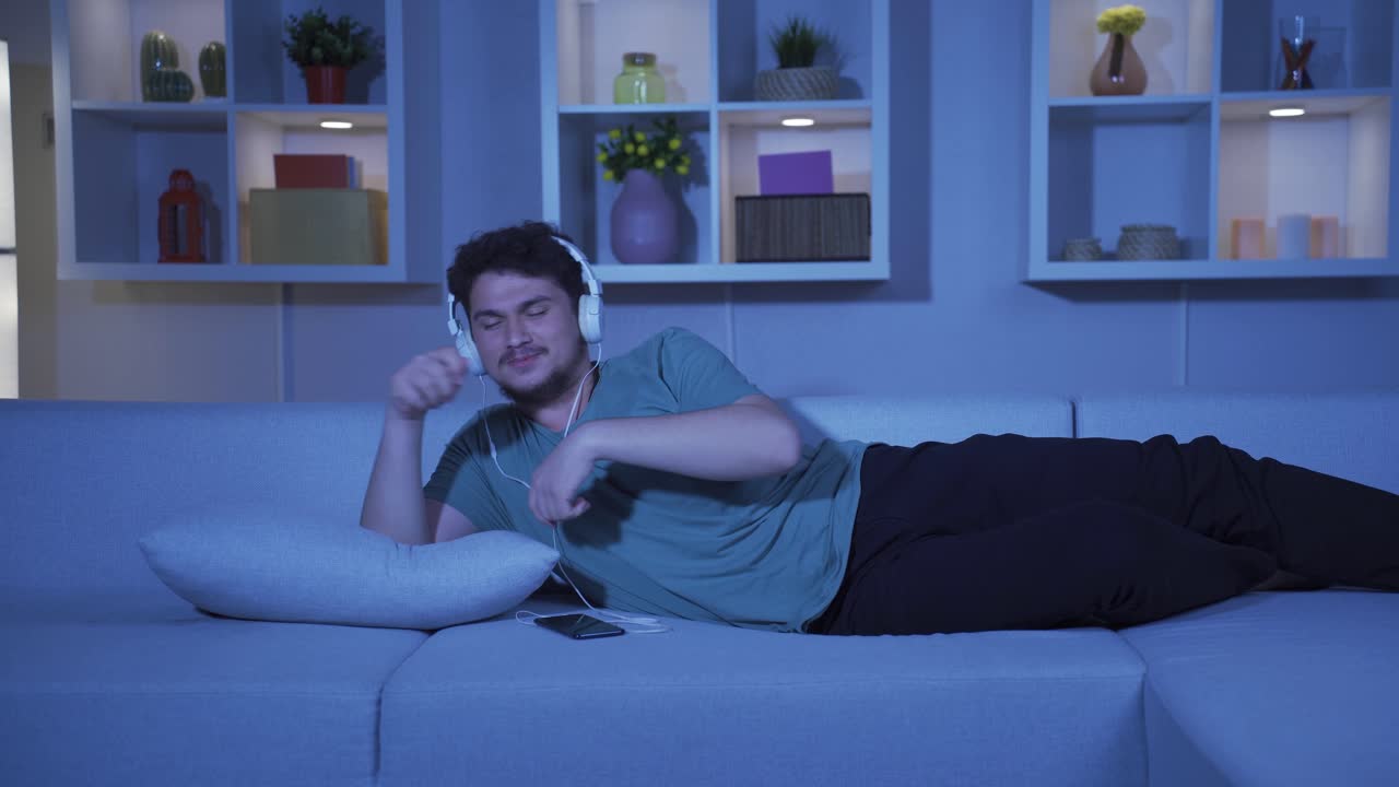 밤에 소파에서 음악을 듣는 남자. 즐겁고 행복합니다.