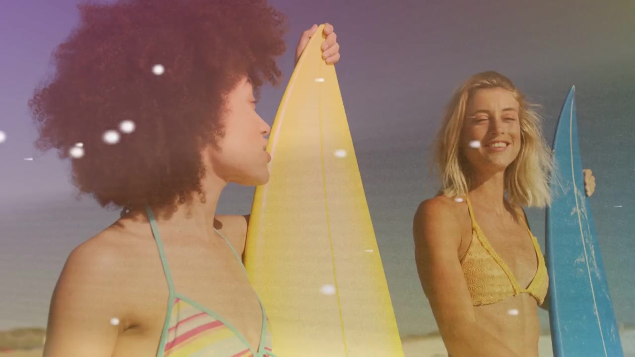 Dos mujeres en la playa observando las olas, señalando y preparándose para surfear entre luces flotantes.