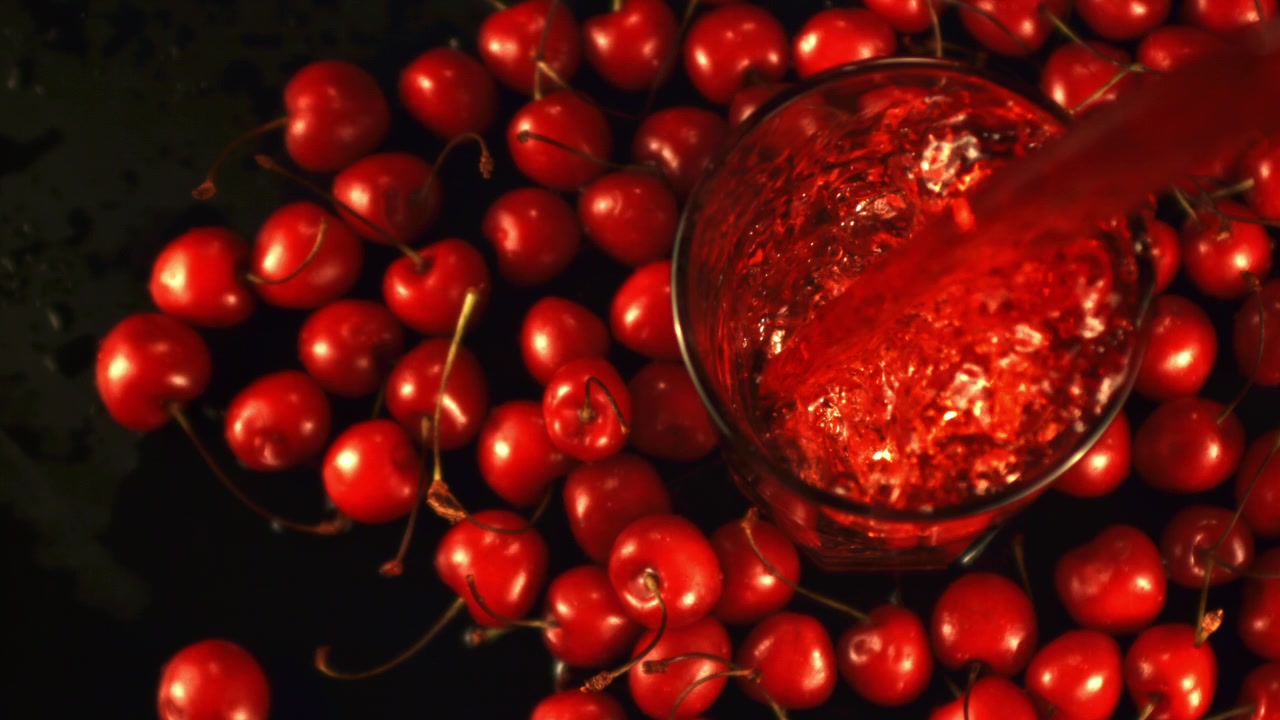 Succo di ciliegia versato in un bicchiere circondato da ciliegie fresche