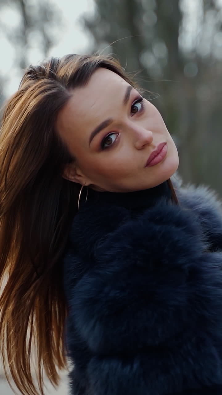 Happy dark haired girl in the park. Young woman in winter coat walking outdoors and drinking hot beverage in a plastic cup. Slow motion. Vertical video