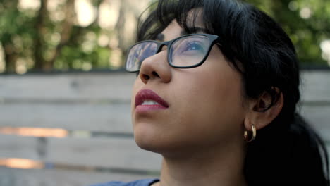 close up of a young latina woman wearing glasses, looking up to the sky on a sunny day