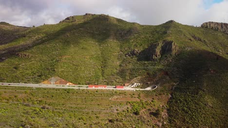 highway road leading into tunnel through mountain in tenerife, aerial view