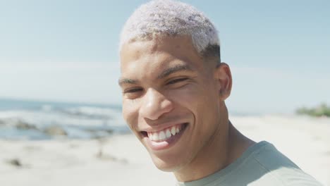 retrato de un hombre biracial feliz sonriendo en la playa, en cámara lenta