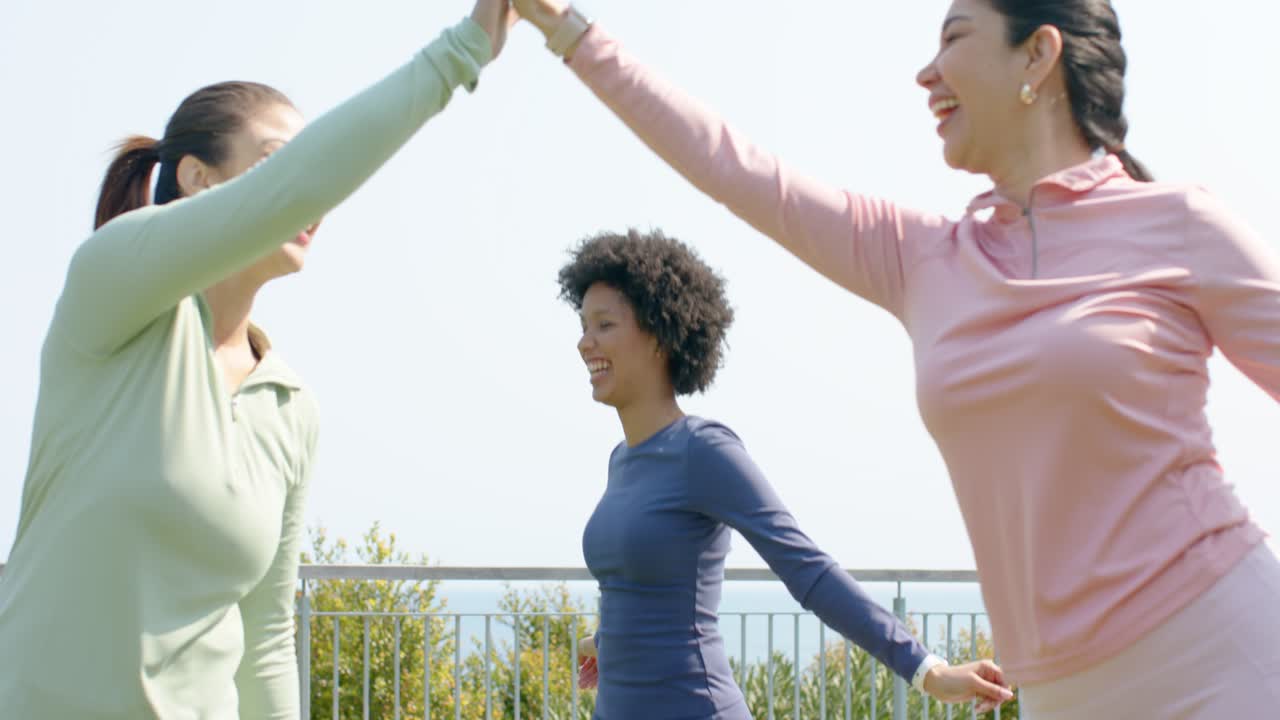 Diverse female workout partners on rooftop upon meeting high-fiving then sharing tips near railing