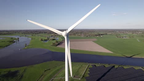 Closeup-of-rotating-blades-of-windmill-turbine-Aerial-of-electricity-generator-with-Twentekanaal-and-river-IJssel-connection-in-the-background