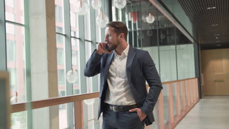 An-Attractive-Young,-Bearded-Businessman-In-A-Blue-Blazer-Has-A-Business-Conversation-With-His-Smart-Phone