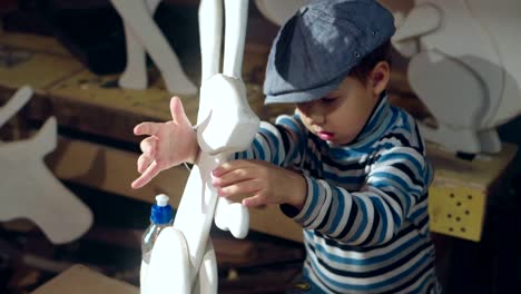 un niño lindo está pegando la oreja a un conejo de juguete en el taller de casa