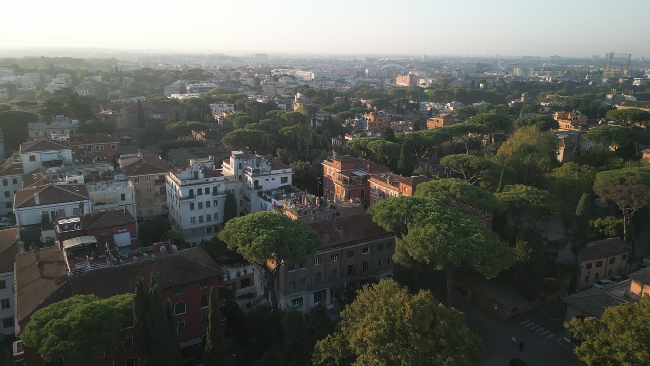 Carrellata di apertura sopra gli alberi verso vecchi edifici storici in mattoni bianchi del Giardino degli Aranci a Roma, Italia.