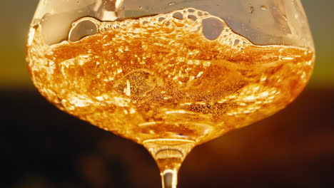 orange or white wine bottle and glass against a sunset in a peaceful vineyard, pouring of ecological natural wine.