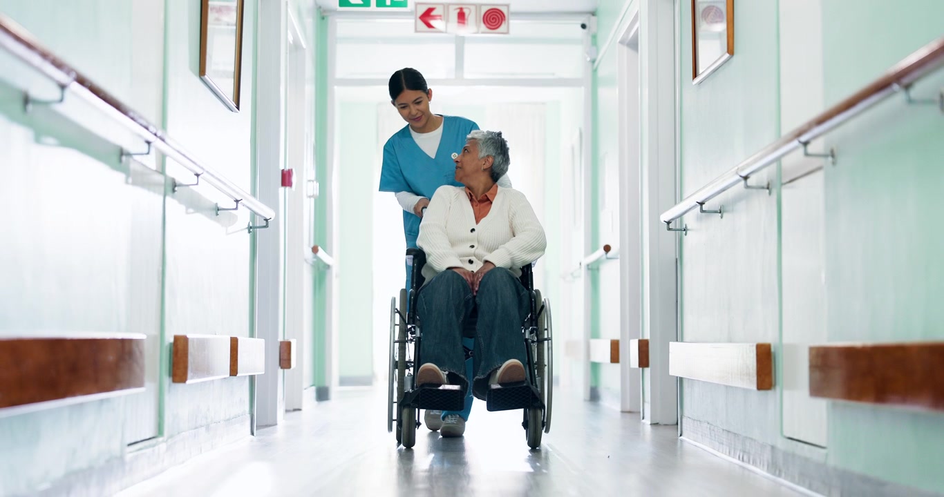 Nurse Pushing Senior Woman in Wheelchair Down Hospital Hallway