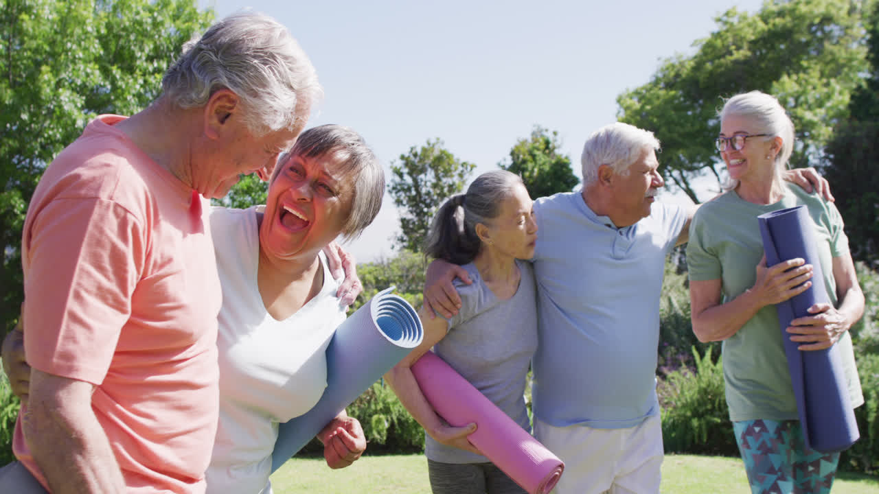 Diverse group of happy male and female seniors talking after exercising in sunny garden, slow motion