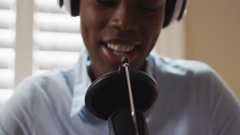 african american woman wearing headphones singing in microphone at home