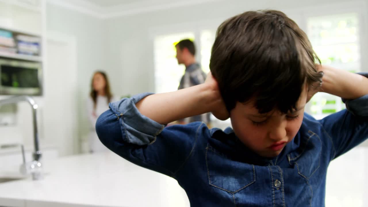 Boy covering his ears while parent quarreling in background