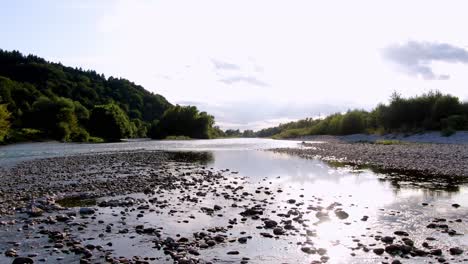 Landscape-view-of-rocks-in-calm-waters-next-to-forest-mountain,-low-altitude-drone-shot