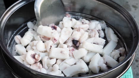 close up shot boiled squid resting on metal strainer, metal spatula mixes