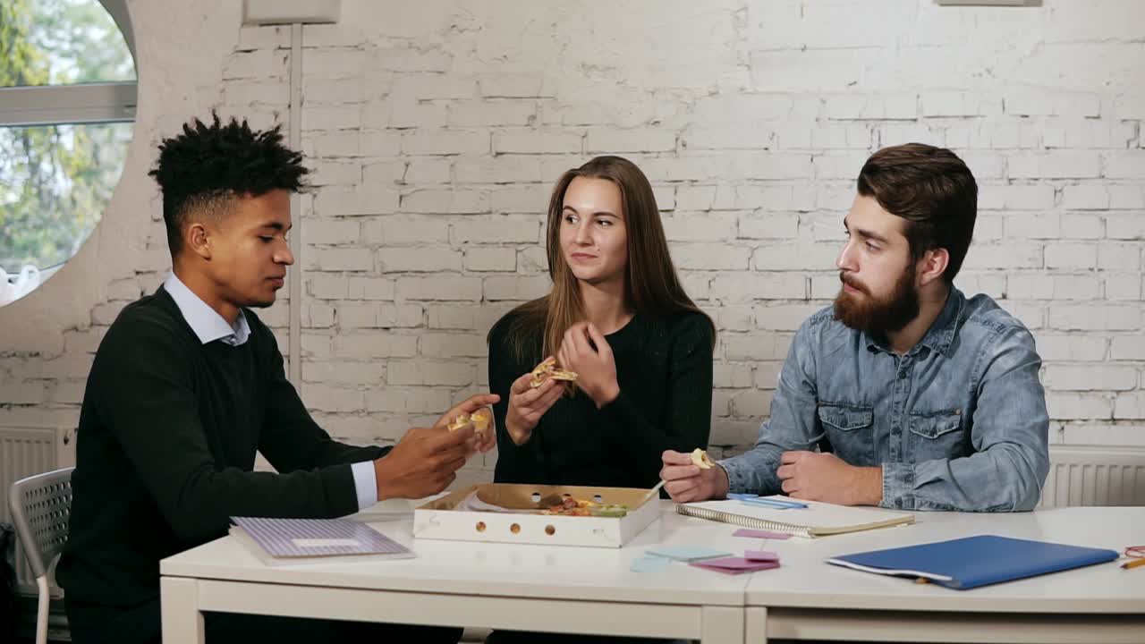 Business team of young people enjoying pizza together in the office, millennials group talking having fun sharing lunch in cozy
