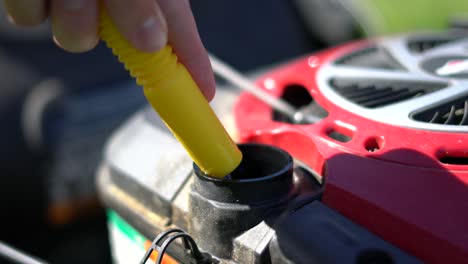 using container with yellow spout to pour gas into lawn mower