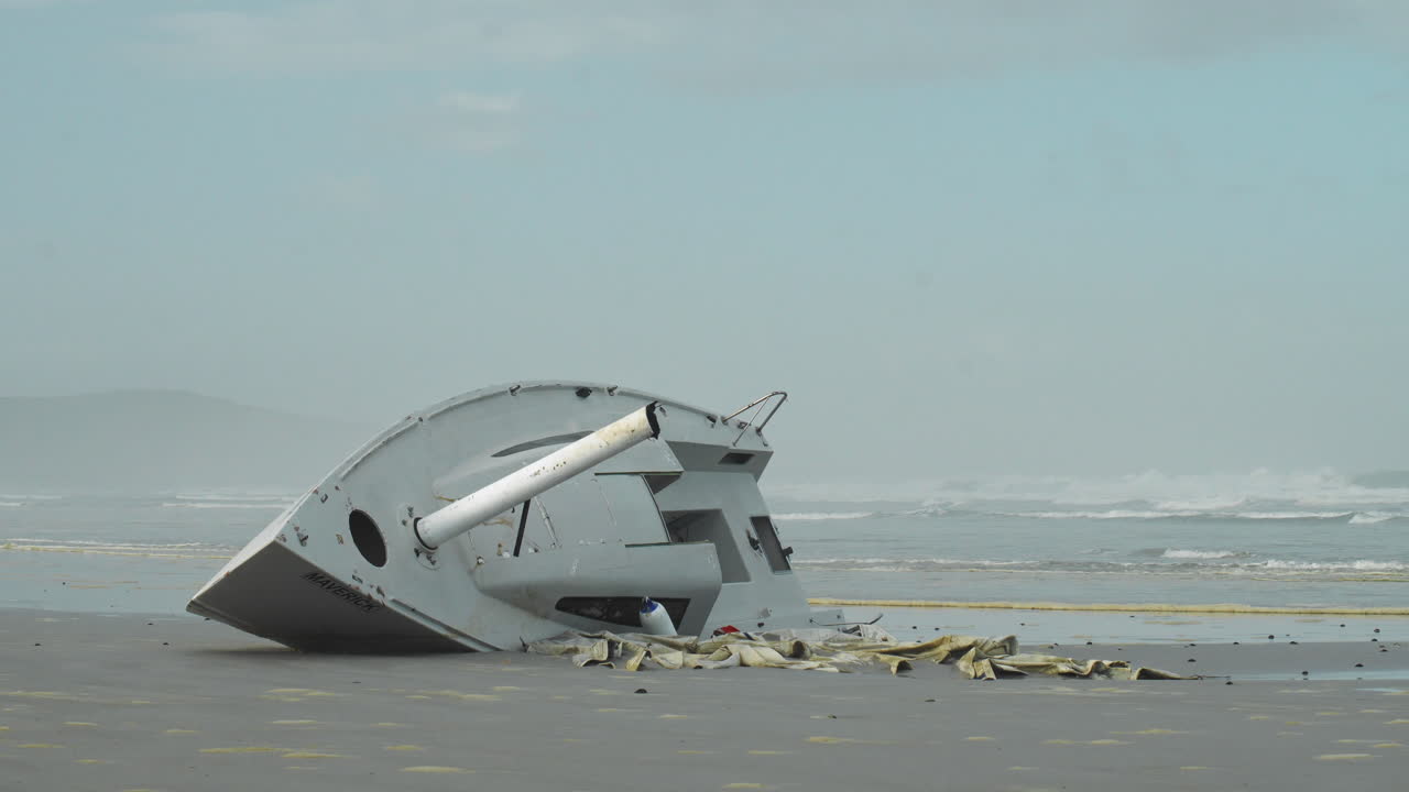 Waves Rushing Past Washed Up Yacht on Gloomy Beach - Wide Static Shot