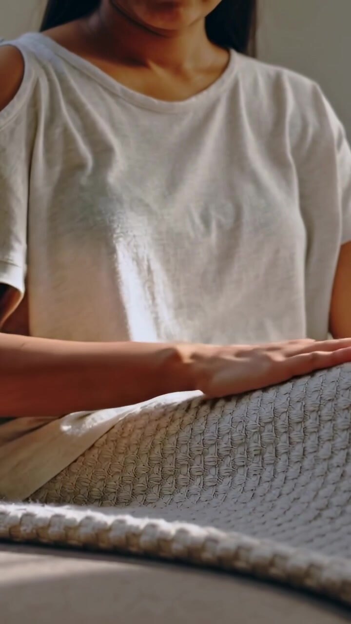 Video verticale: Donna che allunga la mano destra, indossando una maglietta con ritagli, mentre tira e liscia una coperta a maglia sul divano.