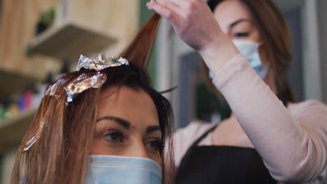 female hairdresser dying hair of female customer wearing face mask at hair salon