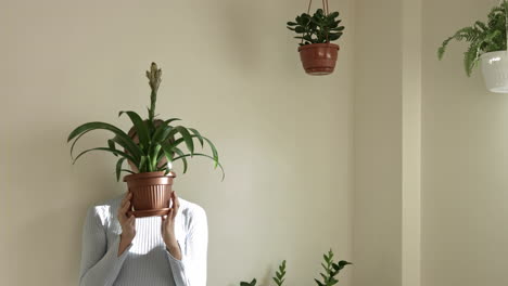 Persona-Femenina-Escondiendo-La-Cara-Detrás-De-Una-Maceta-Con-Planta,-Tiro-Medio-Estático