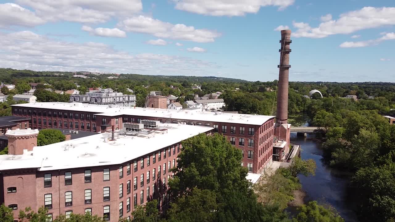 Rising over trees towards an old mill and smoke stack next to the Charles River in Waltham, Massachusetts.