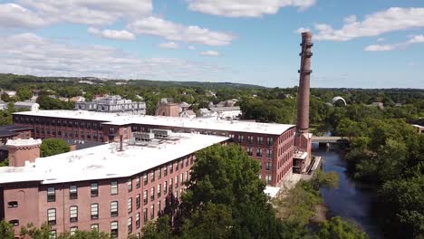 rising over trees towards an old mill and smoke stack next to the charles river in waltham, massachusetts.