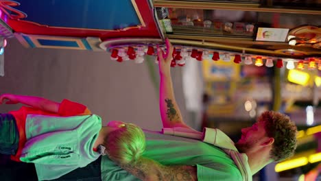 Vertical-video-of-a-happy-dad-with-curly-hair-in-a-green-T-shirt-and-his-little-blond-son-in-a-red-T-shirt-looking-at-the-ticket-office-in-an-amusement-park-and-ordering-tickets-for-themselves