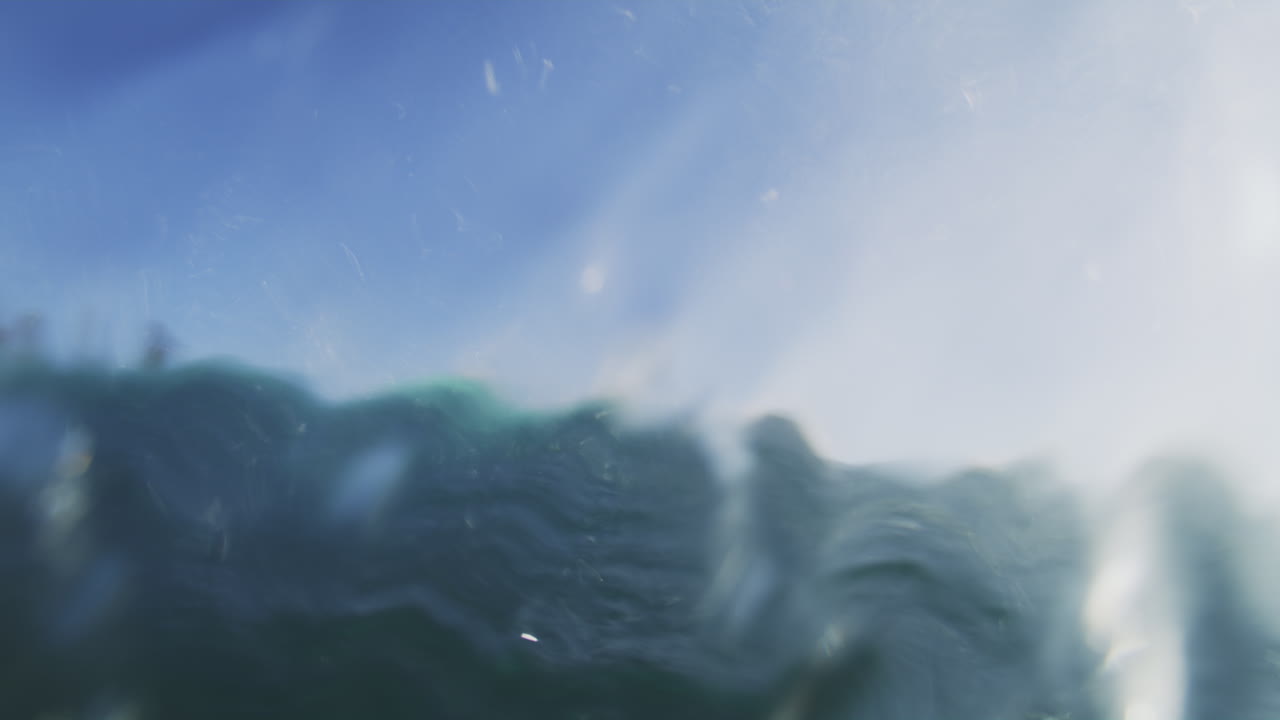 Pan rearview of surfer in barrel through clear water, underwater slow motion view of wave crashing