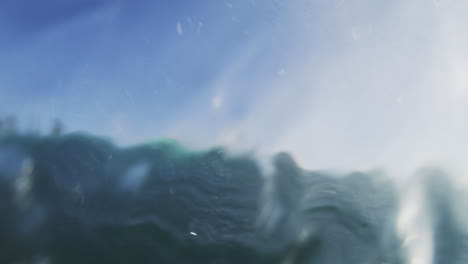 pan rearview of surfer in barrel through clear water, underwater slow motion view of wave crashing