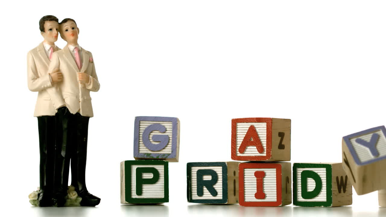 gay novio pastel toppers al lado de los bloques cayendo y deletreando orgullo gay