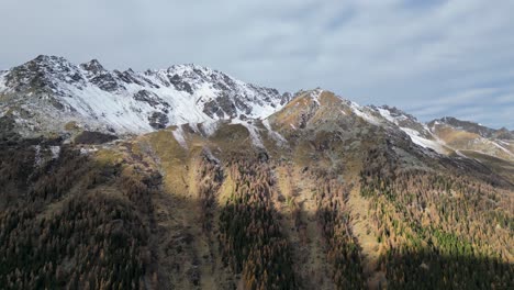 Atemberaubende-Drohnenaufnahmen-Eines-Alpinen-Tals-Im-Herbst-Mit-Verschiedenfarbigen-Bäumen-Und-Einem-Fluss,-Der-Auf-Dem-Talboden-Fließt,-Umgeben-Von-Schneebedeckten-Berggipfeln