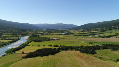 slow drone shot capturing a winding river through vibrant fields, with mountains in the distance. filmed during summertime in norway.