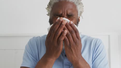 senior man with tissue sneezing in bed at home