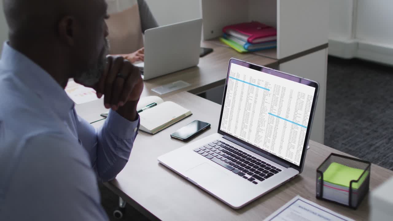 African american man sitting at desk watching coding data processing on laptop screen